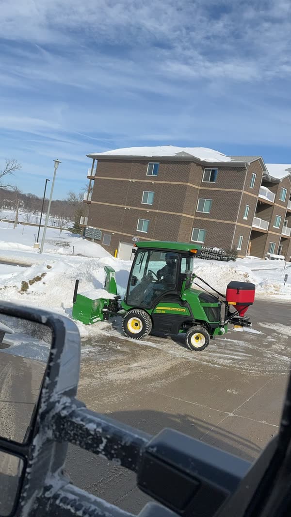 Tractor with a snowblower and spreader clearing an apartment complex lot