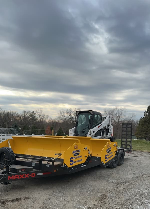 Sectional snow pusher boxes loaded on a trailer with a skid loader