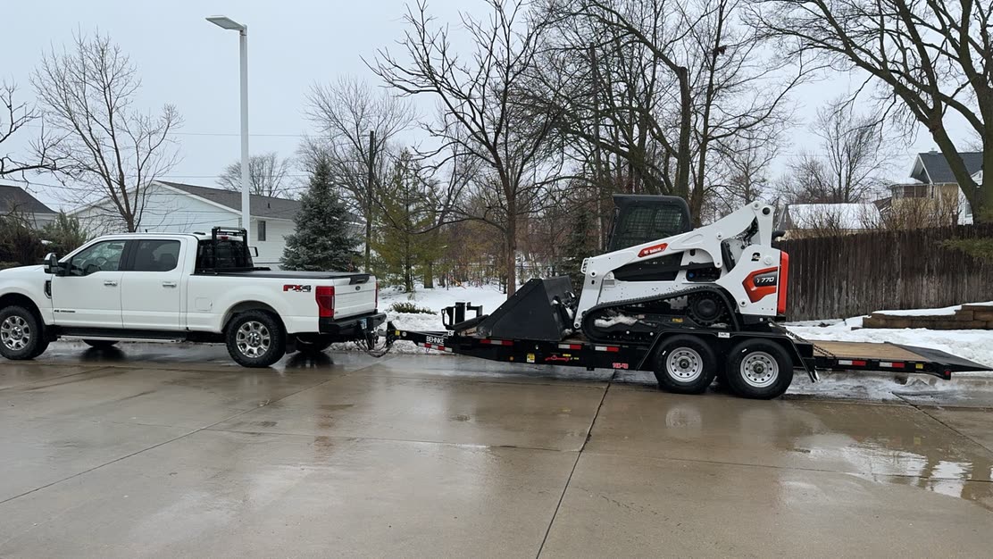 Truck and trailer hauling a tracked loader to a winter job